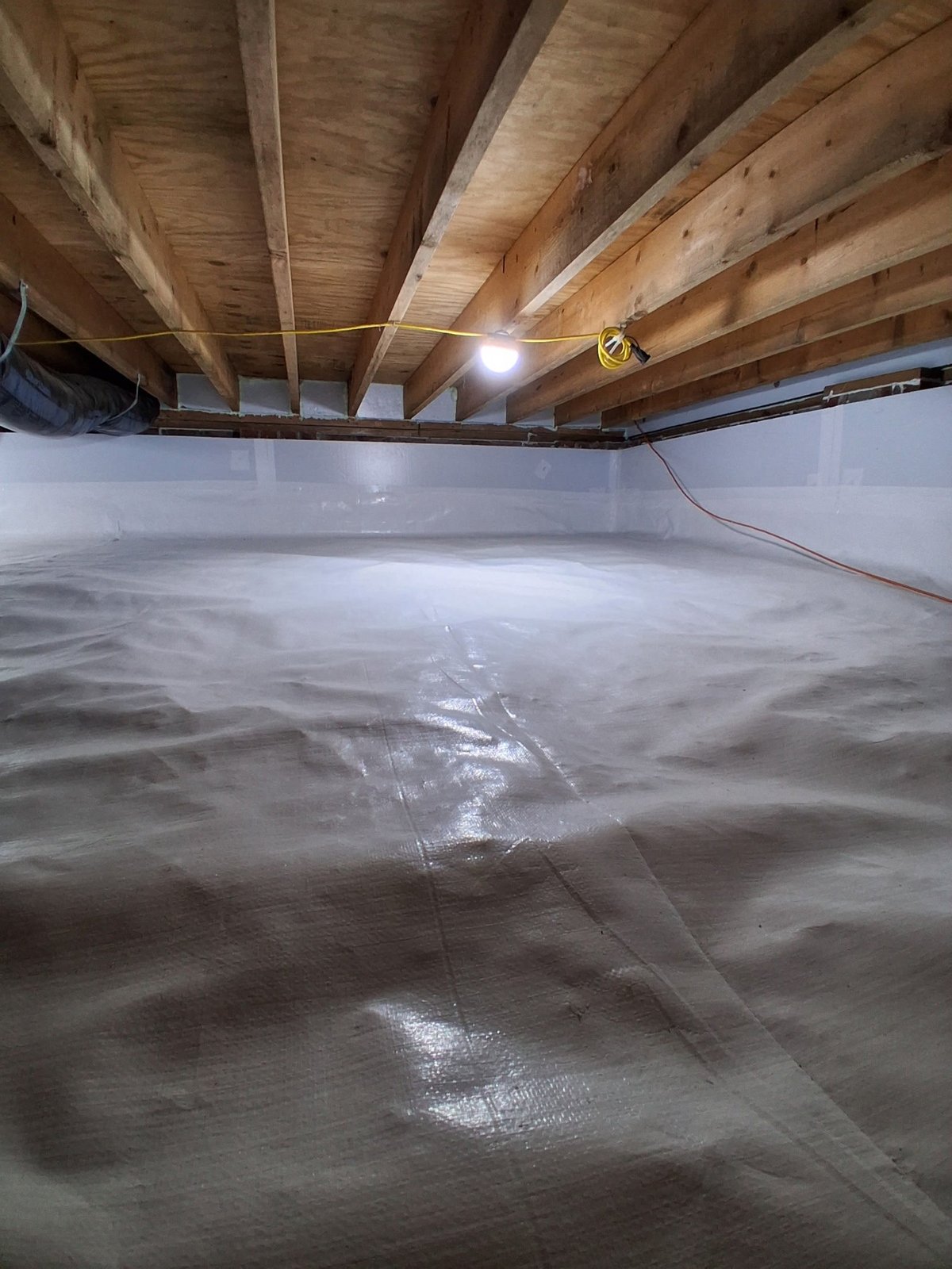 Basement crawl space with plastic vapor barrier on dirt floor and wooden beam ceiling structure overhead