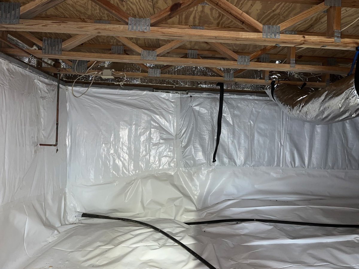 Interior under construction with white plastic sheeting, exposed wooden ceiling beams, and black electrical conduit