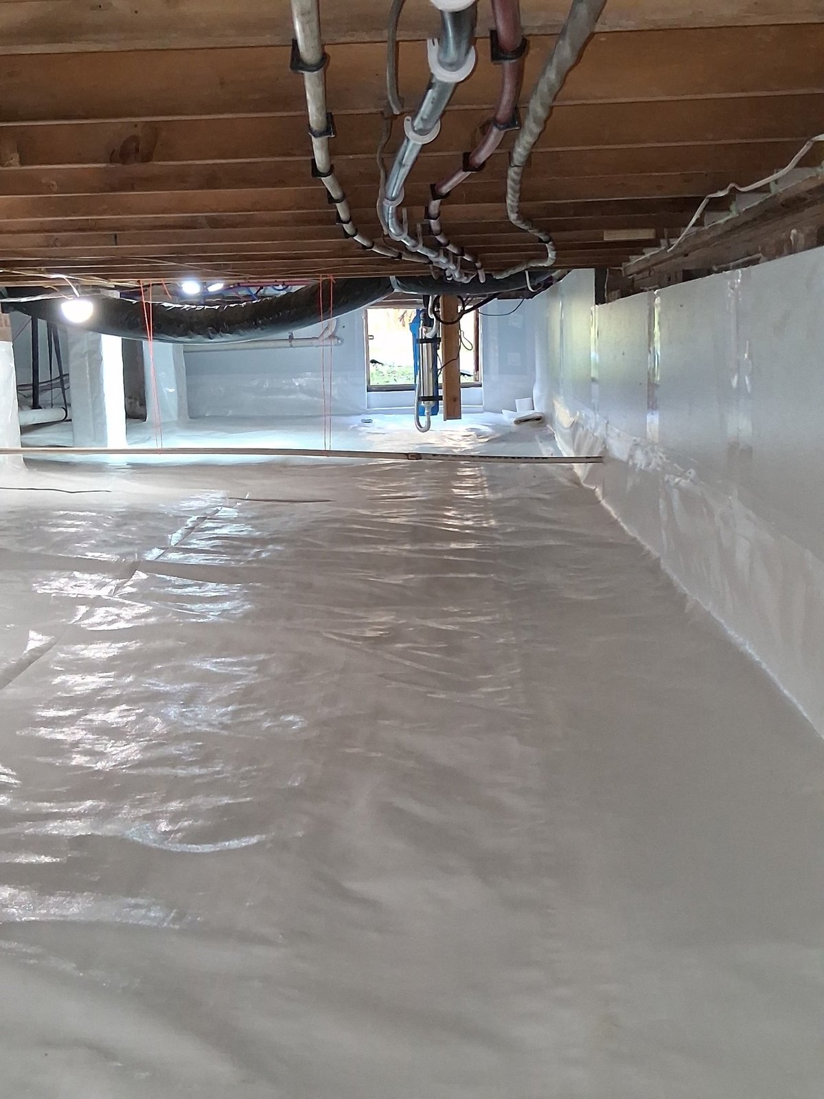 Interior basement space with freshly poured concrete floor, white insulation walls, exposed wooden ceiling beams, and overhead ductwork
