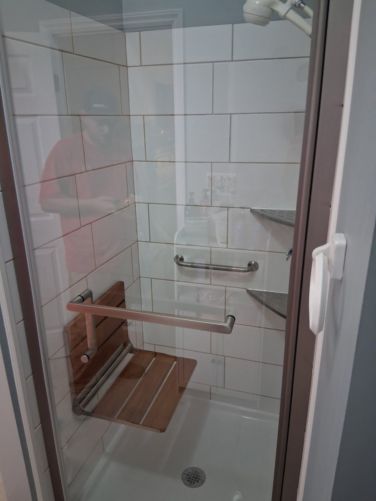 Modern shower stall with glass enclosure, subway tile walls, wooden grab bars, and a built-in shelf
