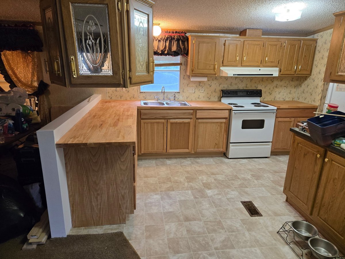 Spacious kitchen with wood cabinetry, tile flooring, island counter with white trim, and white electric stove