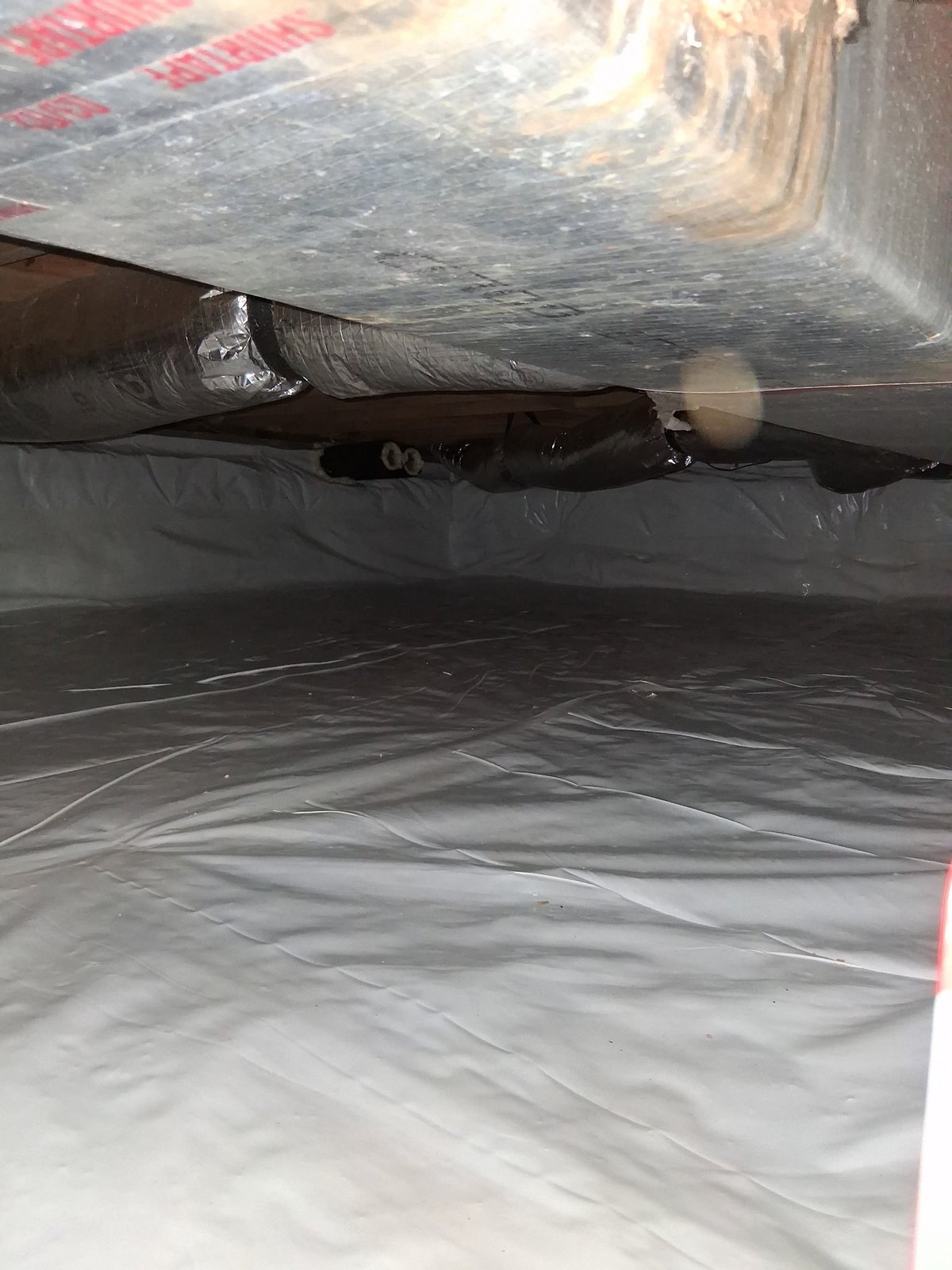 Underside of vehicle showing exposed axle and suspension components against plastic ground sheeting