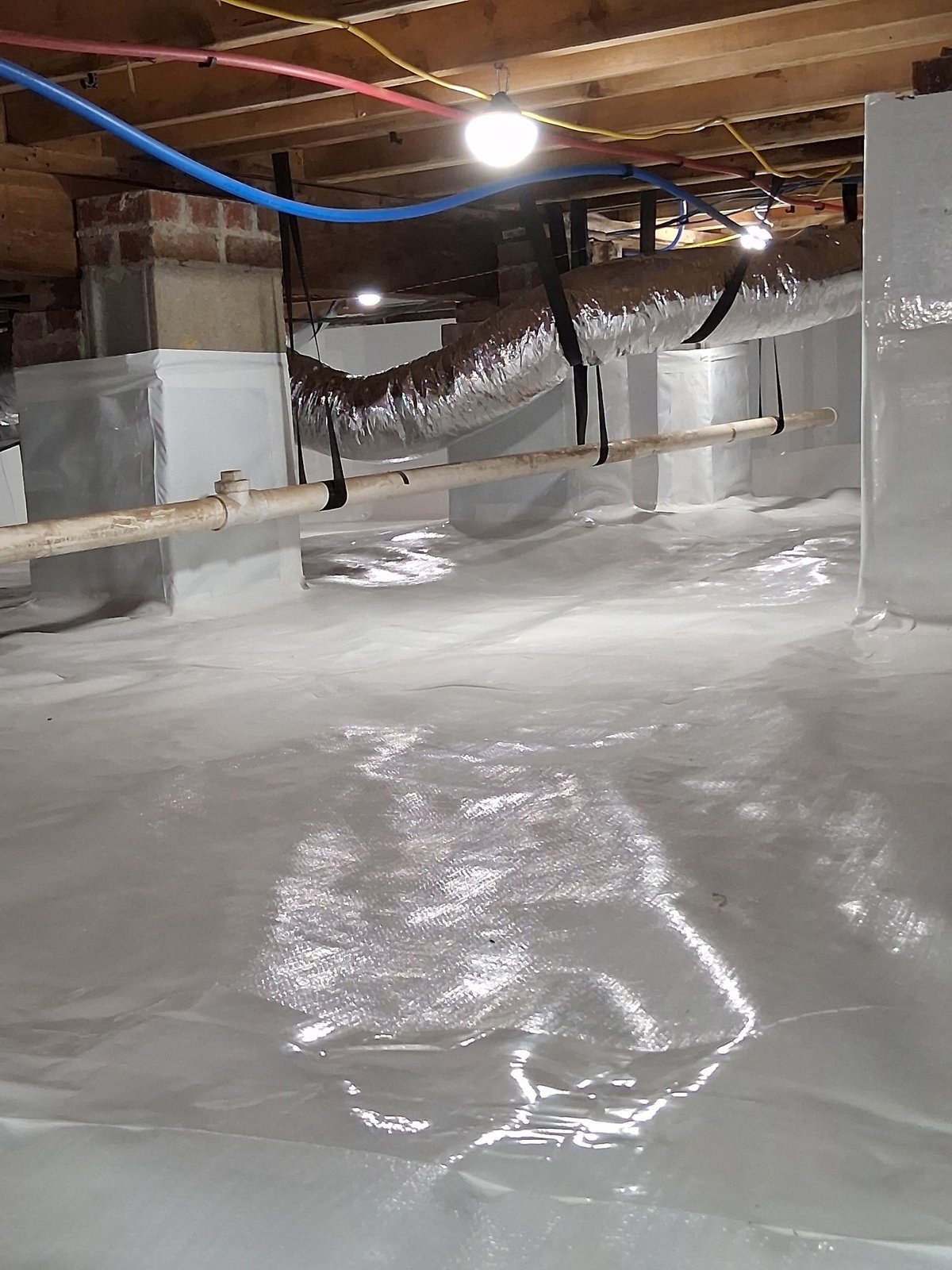 Unfinished basement with white moisture barrier flooring, exposed ducts, and construction materials